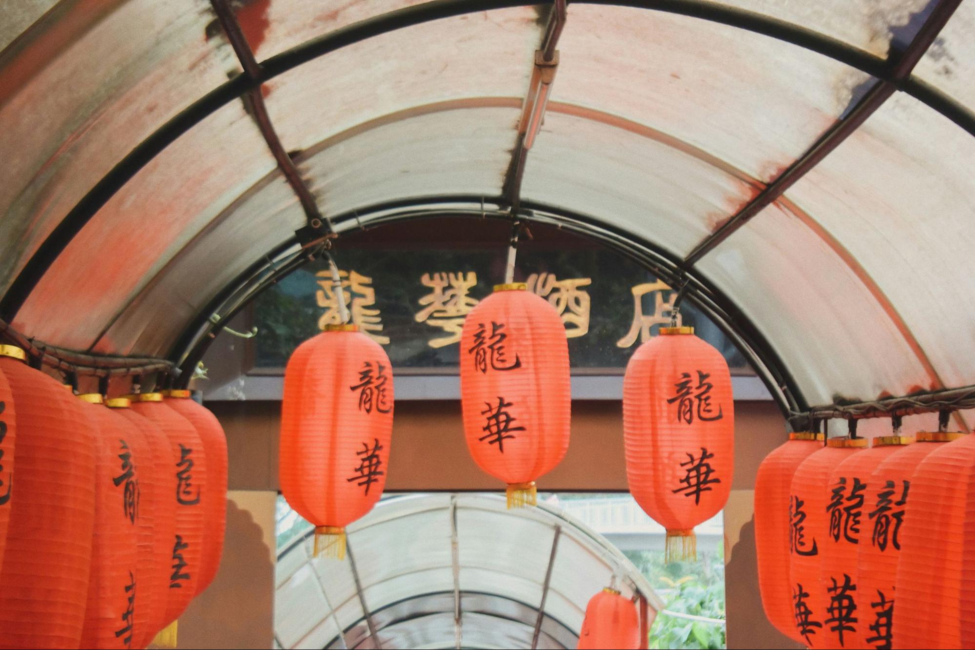 Red Chinese lanterns with black characters hang under a curved, transparent roof structure.